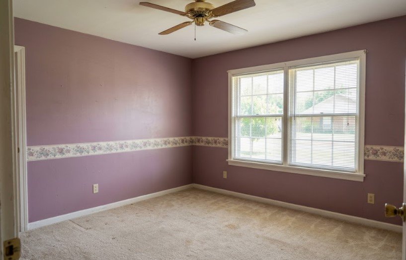 Bedroom with dated mauve walls and a floral wallpaper border before repainting