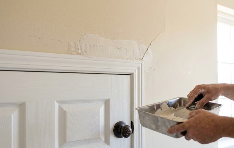 Painter applying joint compound over mesh tape on a drywall crack above a door frame