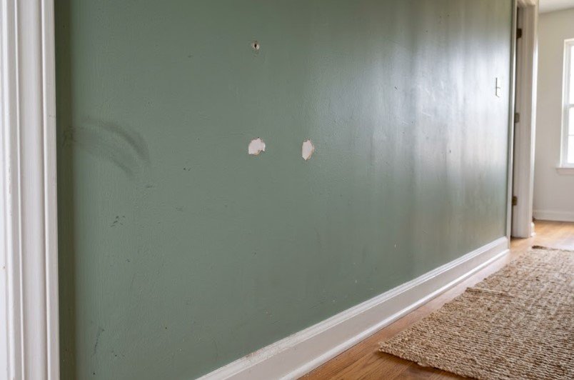 Two paint chips and a nail hole in a sage green hallway wall