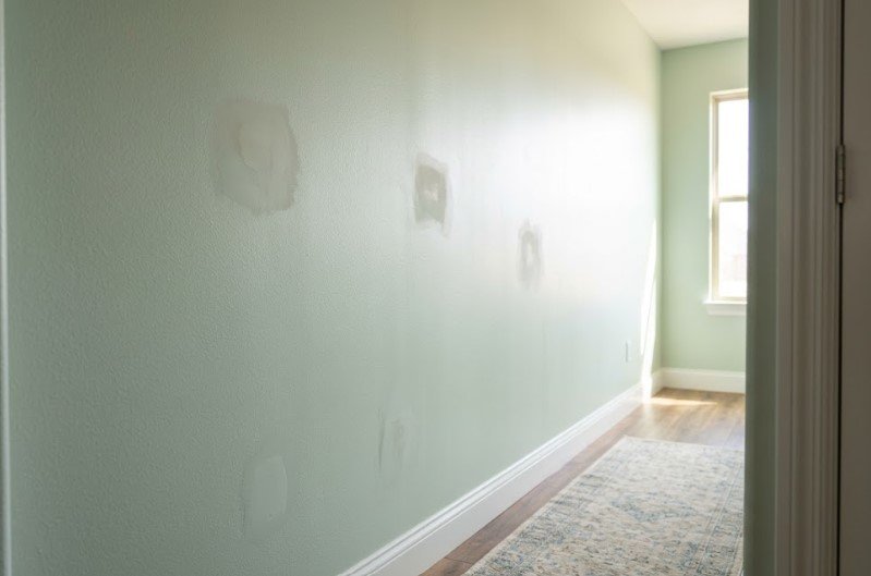 Dull patches over drywall repairs on a mint green hallway wall, seen in side light from a window